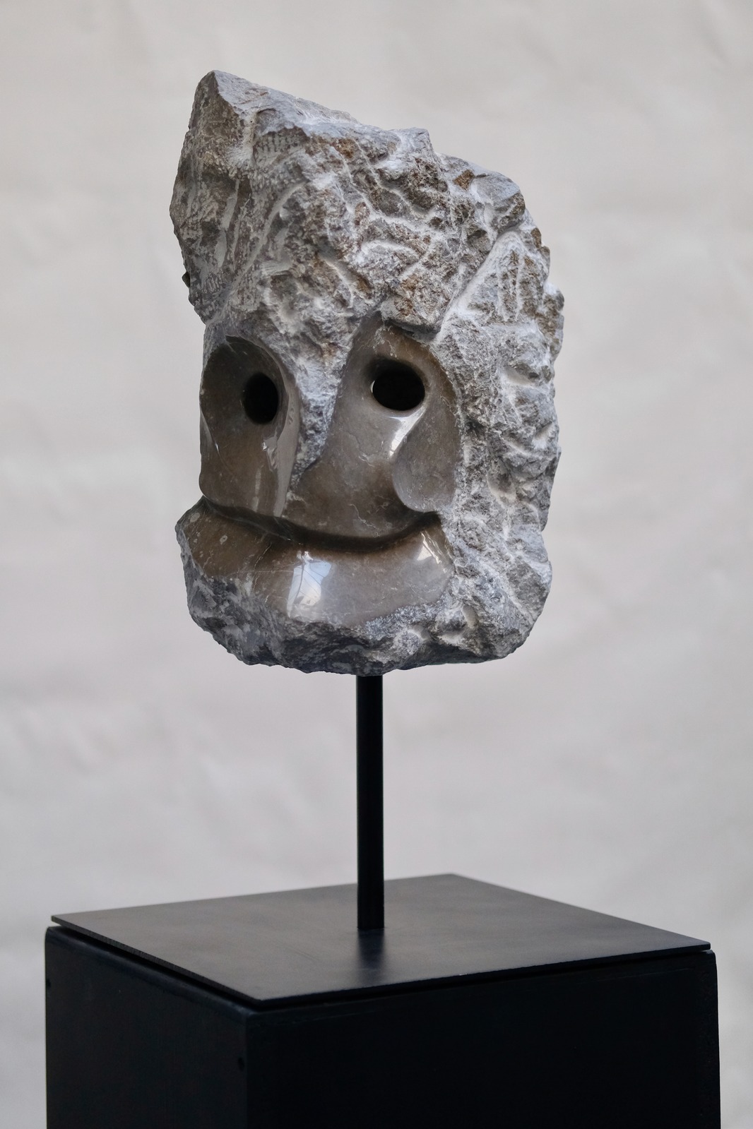 KAIROS, a carved limestone face with polished planes and a raw stone crown, mounted on a black plinth